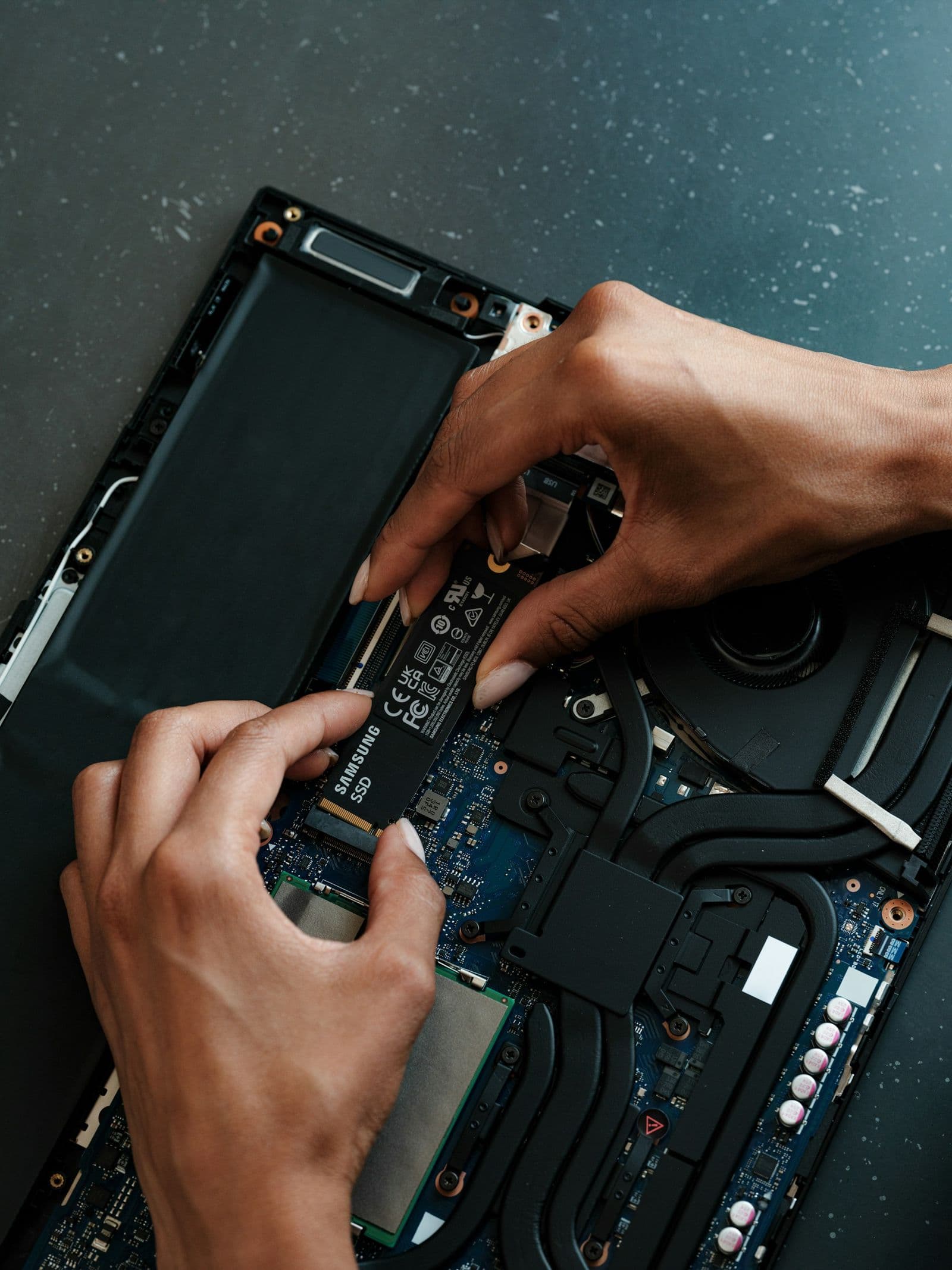 Hands seating an NVMe drive into a laptop mainboard