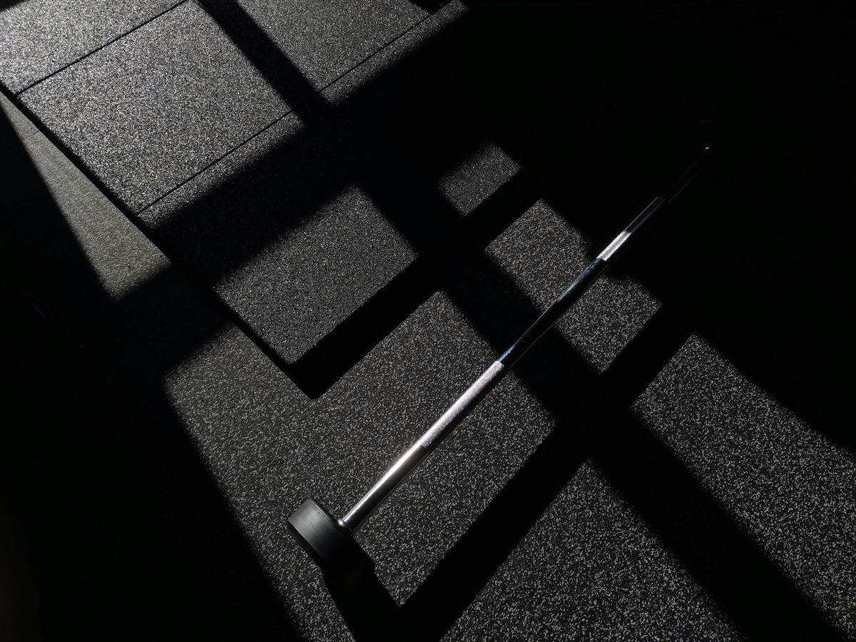 A barbell on rubber floor in shadow
